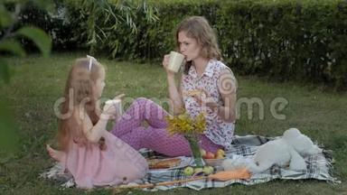 一对幸福的母女正在面纱上喝茶.. 一家人在城市公园里，在日落的温暖的晚上野餐。
